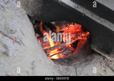 Close up shot featuring the orange flames and gray ashes of burning wood inside a pit dug in the dirt. It conveys the concepts of fire, heat and energ Stock Photo