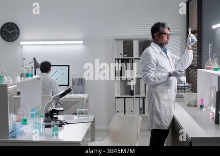 Researchers working in modern science lab, using microscopes and test tubes, analyzing samples and chemicals, surrounded by laboratory equipment and technology Stock Photo