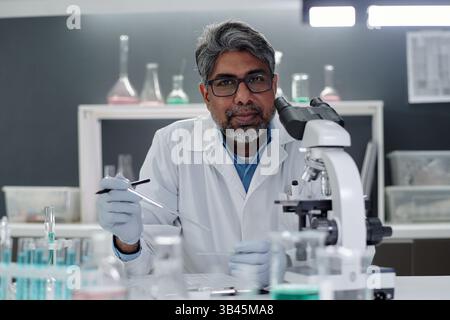 Portrait of scientist examining samples with precision equipment in modern laboratory. Senior researcher concentrating on experimental procedures while wearing lab coat and glasses Stock Photo