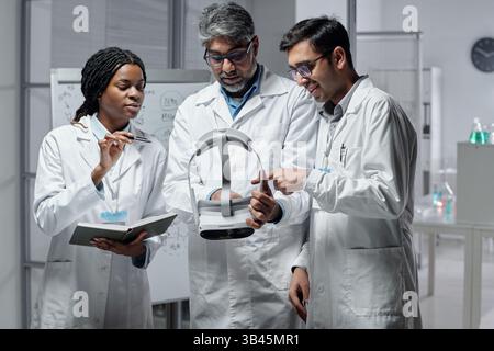 Group of diverse scientists discussing new medical device in laboratory. Multi-ethnic team collaborating on innovative technology for healthcare research and development Stock Photo