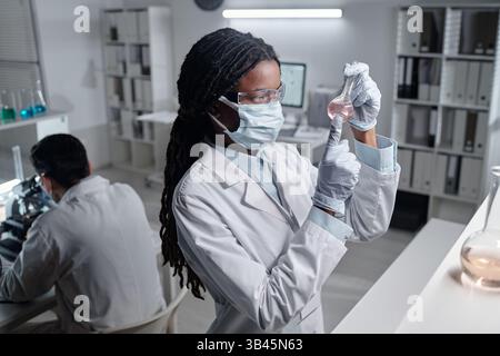 African American scientist analyzing liquid in flask while wearing protective gear and working in well-equipped lab environment Stock Photo