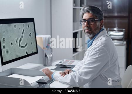 Portrait of doctor with salt and pepper beard looking at camera while analyzing a microscopic image on computer screen during research in laboratory Stock Photo