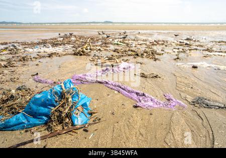 Polluted beach landscape showing discarded plastic waste and garbage scattered across coastal sand, environmental impact revealing marine ecosystem Stock Photo