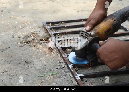 Dark-skinned person cutting steel with a grinder, sparks, outdoors. Professional uses angle grinder on metal grid for fabrication. Stock Photo