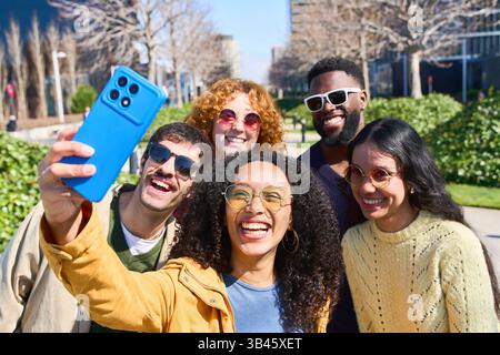 Cheerful multi ethnic group of young adult friends smiling and taking a selfie with a smartphone in the city Stock Photo