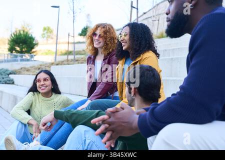 Happy multiethnic students enjoying their free time together, sitting on campus steps, engaging in lively conversation and sharing laughter Stock Photo