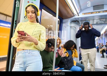 Passengers using smartphones and listening to music through headphones while commuting on a subway train Stock Photo