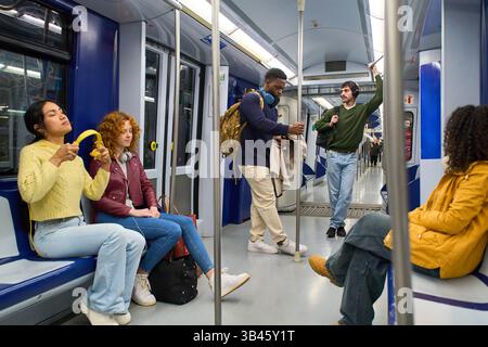Passengers using public transport, listening to music, and holding onto handrails during their commute Stock Photo