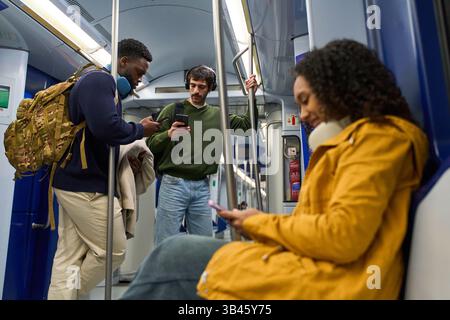 Passengers using their smartphones while traveling on a subway train, engrossed in their digital world Stock Photo