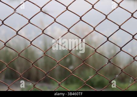 Close-up shot featuring a rusted chain link fence with a blurry out-of-focus background, forming a repeating pattern, adding visual depth to the compo Stock Photo