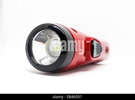 A vivid red and black flashlight with a gray button on a white background. The flashlight emits a bright light with a clear lens. Stock Photo