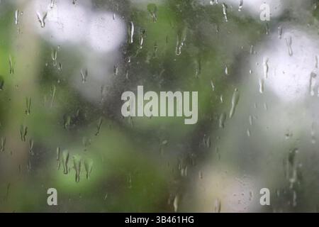 Close-up captures water droplets on the misted glass with blurry background from the window view on a rainy day, perfect for conveying weather concept Stock Photo