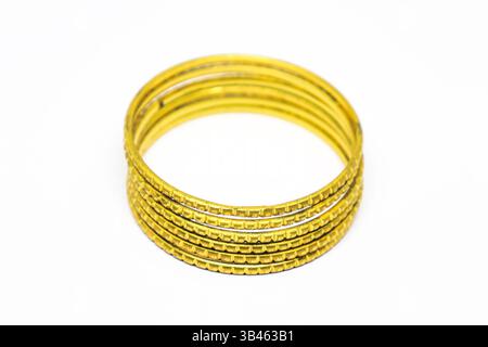 Features a close-up of stacked gold bangles with textured designs on a white surface. The jewelry reflects light, highlighting craftsmanship. Stock Photo