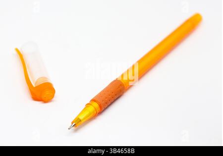 Close-up photograph featuring an open, orange, ballpoint pen with a textured grip alongside its cap resting on a white background, ideal for writing p Stock Photo
