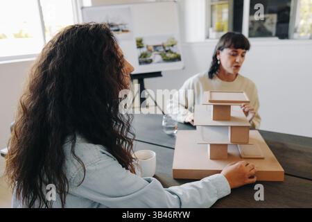 Two women are collaboratively discussing and presenting a creative three-dimensional architectural model design in a professional setting, reflecting Stock Photo