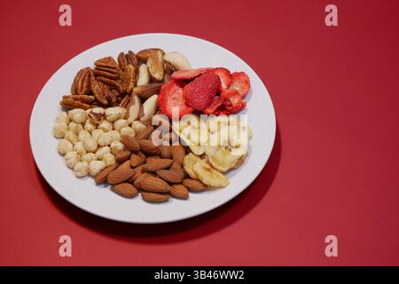 A variety of nuts and dried fruits on a plate on red background. Hazelnuts, pecans, brazil nuts, almonds, dried strawberries and bananas. The concept Stock Photo