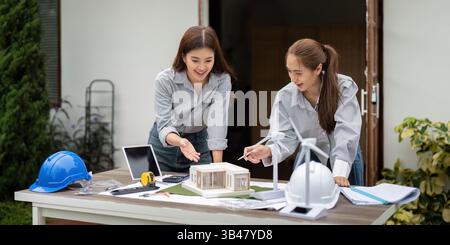 Sustainability and Architecture. Two architects discussing eco-friendly building designs with a model and wind turbines. Stock Photo
