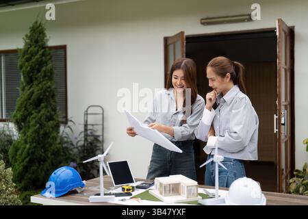 Sustainable Architecture Discussion. Female architects examining eco-friendly building plans and models. Stock Photo