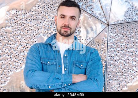 Confident man in denim shirt standing with crossed arms against abstract wall Stock Photo