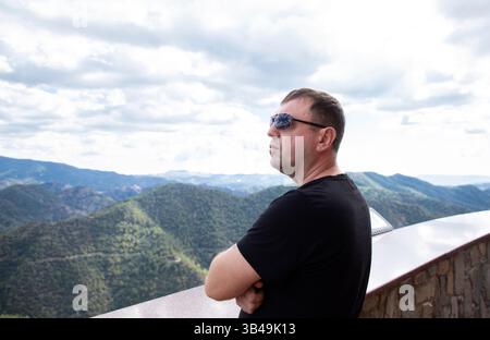 man in profile, 35-40 years old, stands on a viewing platform and admires the surrounding landscape Stock Photo