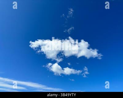 Fluffy white clouds drift against a bright blue sky on a beautiful, sunny day. Stock Photo
