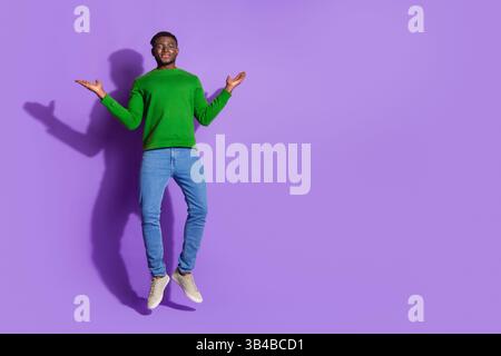Confident young man jumping in casual attire on a vibrant purple background Stock Photo