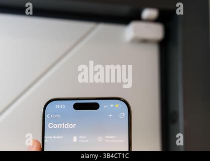 A close-up of a smartphone displaying a smart home interface, showing real-time security status with Door Sensor in Background Stock Photo