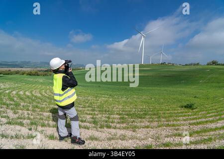 Female engineer controlling wind turbines with drone in green field Stock Photo
