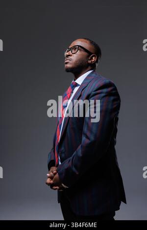 Thoughtful businessman in striped suit and glasses, looking up with hand on chin. Concept of decision-making, planning, strategy, leadership, and inno Stock Photo