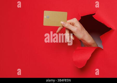 Close up of woman holding mockup of golden bank credit card with online service on red background. Stock Photo