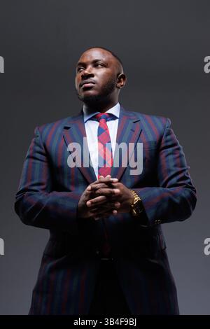 Confident businessman in a stylish striped suit and tie, posing with hands clasped. Professional portrait, leadership, success, corporate style, autho Stock Photo