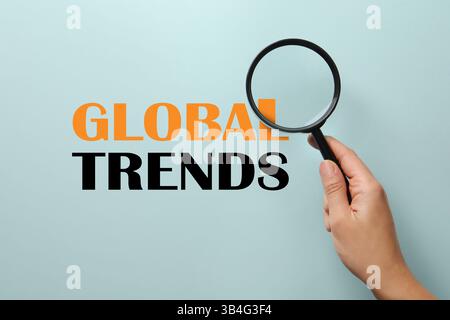 Words Global Trends, view through magnifying glass in woman's hand Stock Photo
