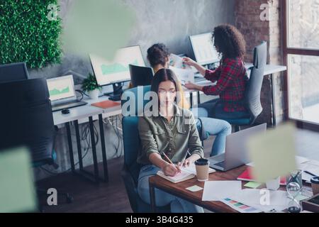 Young focused professionals collaborating in a modern coworking space with green decor, working on project Stock Photo