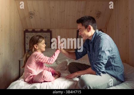 Father and daughter playing together in the bedroom. Father and daughter giving high five to each other. Stock Photo