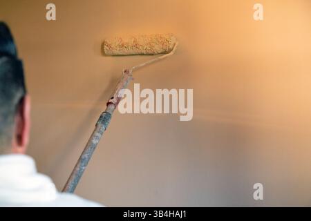 Close-up of person using roller brush to paint a wall in warm tones during interior renovation. Stock Photo