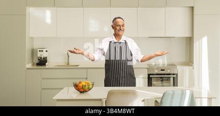Mature man in a black and white apron standing in a kitchen Stock Photo