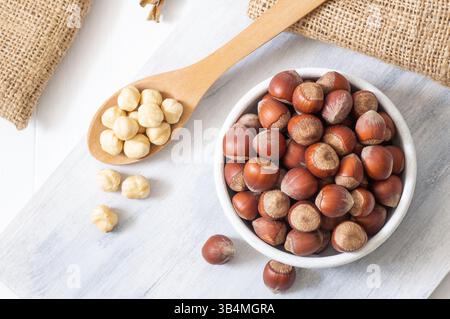 Hazelnut, whole and peeled hazelnuts in bowl and wooden spoon on white bright table, healthy food Stock Photo