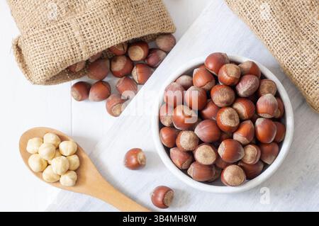 Hazelnut, whole and peeled hazelnuts in bowl and wooden spoon on white bright table, healthy food Stock Photo