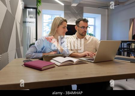 Two colleagues working together on a laptop in a modern office setting Stock Photo