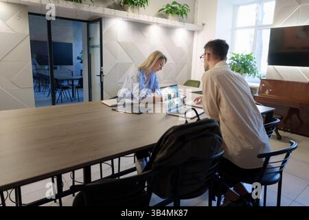 Two colleagues collaborating over a laptop in a modern workplace setting Stock Photo