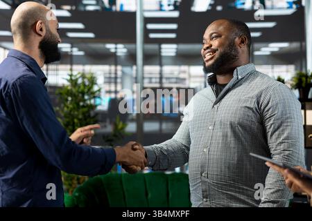Smiling Middle Eastern interviewer holding meeting with job candidate, doing handshake, asking questions and presenting company background. Jolly Arab HR employee interviewing man Stock Photo