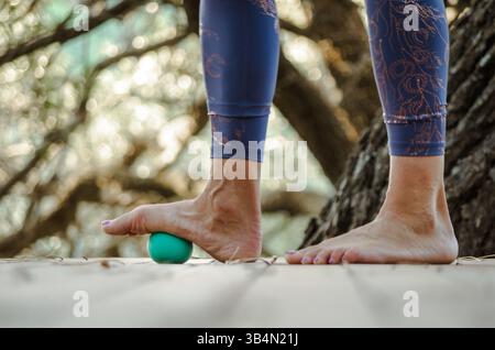 Woman practicing foot myofascial release on outdoor yoga platform Stock Photo
