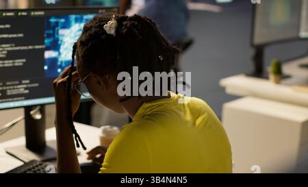 Staff member in office yawning during shift, feeling tired while looking at artificial intelligence software on PC. Exhausted african american AI company employee being sleepy in workspace, camera A Stock Photo