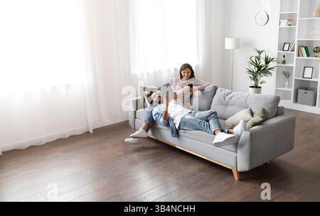 Mixed race spouses resting on sofa at home, using gadgets Stock Photo