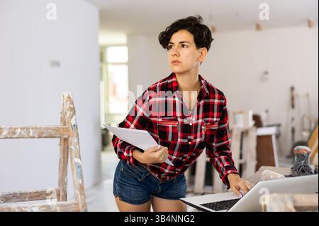 Woman builder checking project documentation and using laptop while working Stock Photo