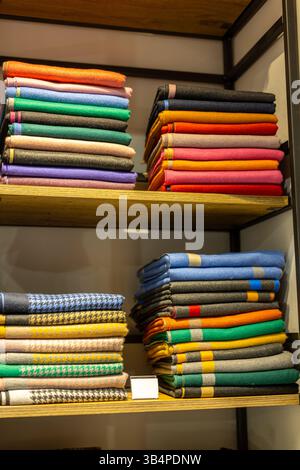 Neatly arranged stacks of colorful fabrics in various shades are displayed on wooden shelves inside a textile store. The vibrant colors create an invi Stock Photo