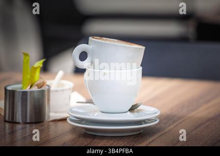 Two empty used espresso cups, coffee cups, stacked rim-to-rim on saucers with spoons rest on a wooden cafe table, illustrating break time after coffee Stock Photo