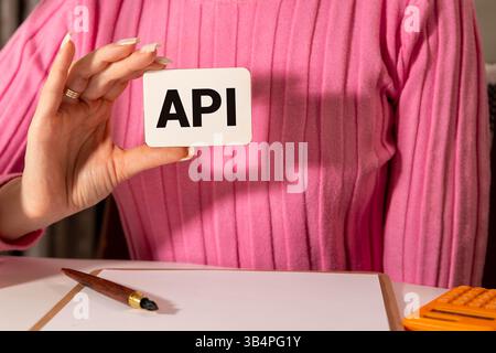 On a table, a magnifying glass and pen are positioned among yellow envelopes, highlighting a card prominently featuring the text API, indicating a foc Stock Photo