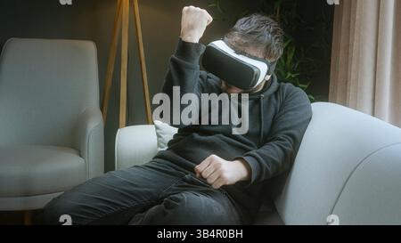 Man Playing a Shooting Game Using VR Headset While Sitting Comfortably at Home Stock Photo