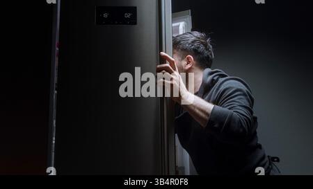 Young man taking cooking ingredients from fridge at night in modern kitchen Stock Photo